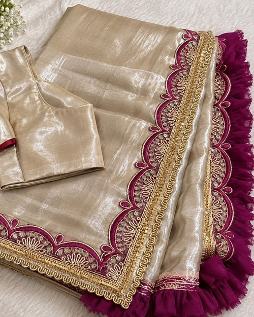 Beige cotton blend tissue saree laid flat with its matching unstitched blouse piece, showing the magenta scalloped embroidered border and ruffle edging