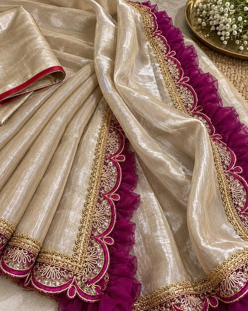Close-up of the beige cotton blend saree showing the gold and magenta scalloped lace border with ruffle trim against the shimmering tissue fabric