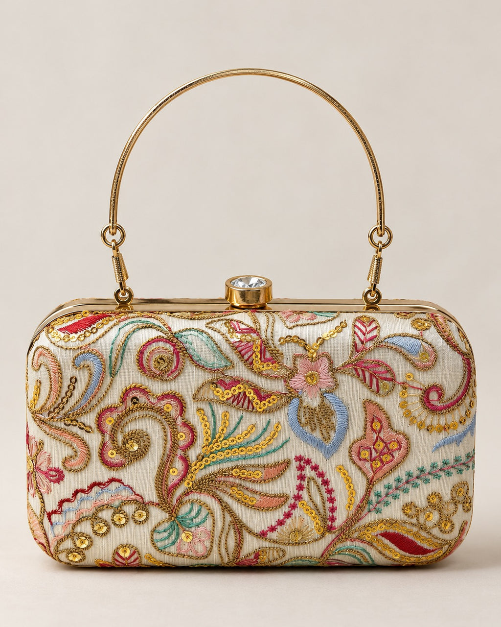 Embroidered box clutch with gold top handle on a plain off-white background