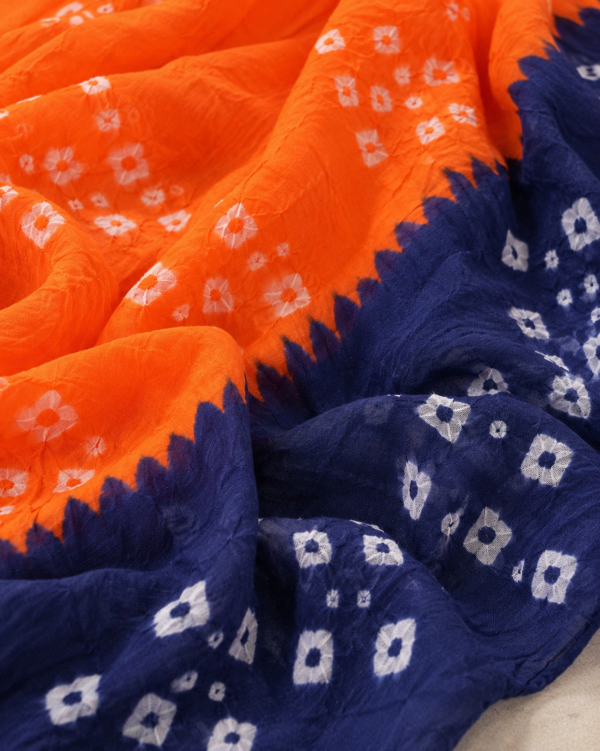 Close detail of the white bandhani tie-dye motifs where the orange body meets the navy border