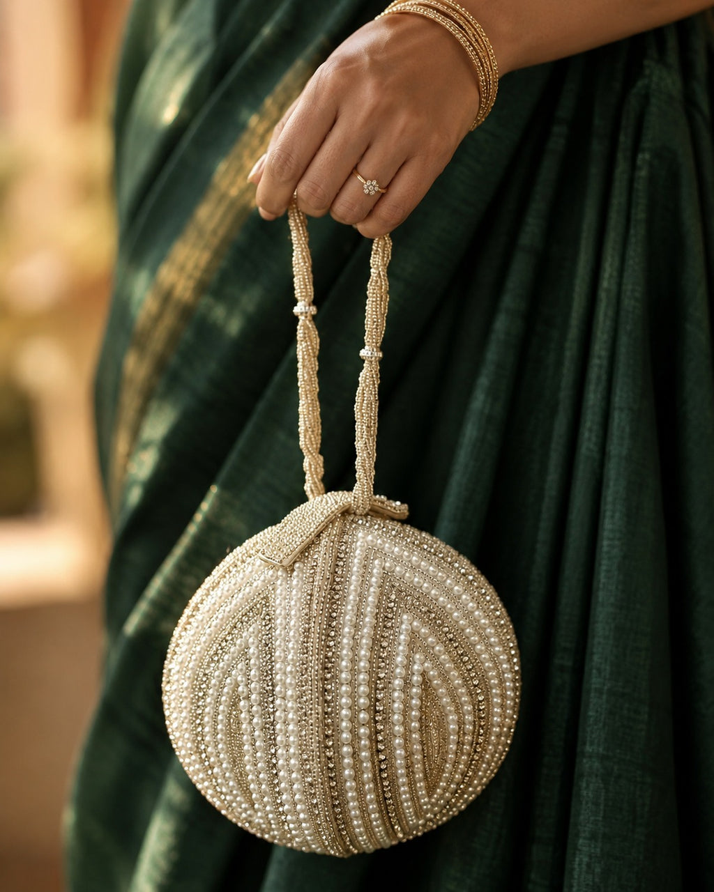 Pearl shell potli clutch with gold chain sling held in hand against an emerald silk saree