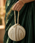 Pearl shell potli clutch with gold chain sling held in hand against an emerald silk saree